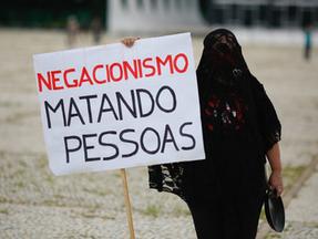 Mulher vestida de preto segurando cartaz contra negacionismo