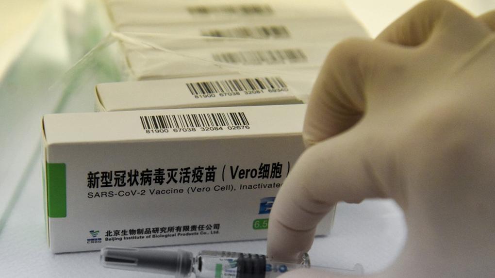 Mão segurando seringa com vacina da Sinopharm em frente a caixas do imunizante
