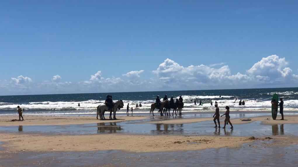 Equipe de cavalaria da Polícia Militar em meio a pessoas na faixa de areia da Praia do Futuro