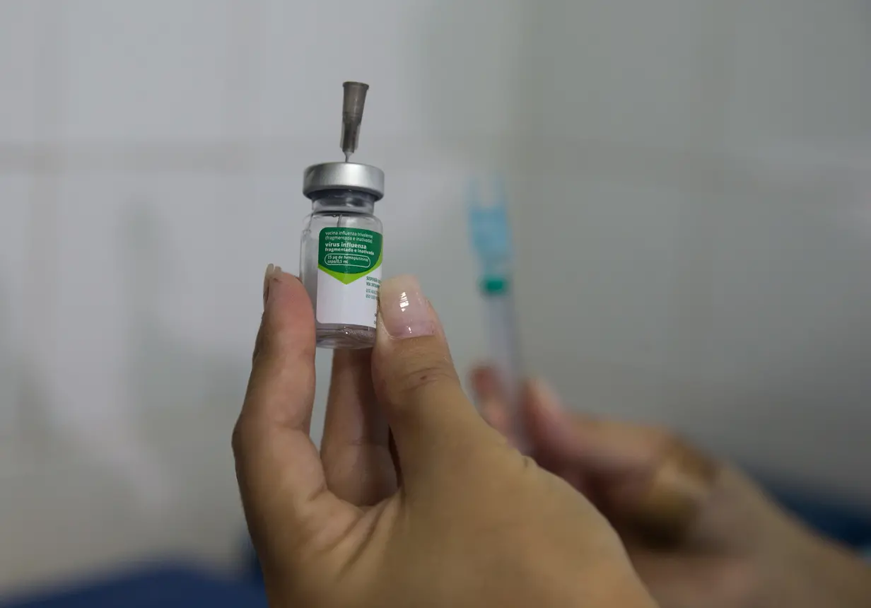 Imagem mostra uma mãe segurando um frasco contendo dose da vacina contra a gripe