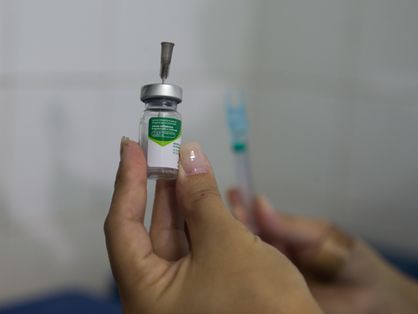 Imagem mostra uma mãe segurando um frasco contendo dose da vacina contra a gripe