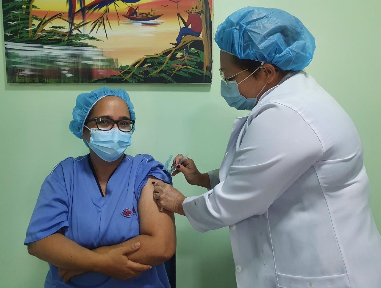 Nancy Costa, à dir., vacinando contra a Covid-19 uma de suas colegas de profissão.