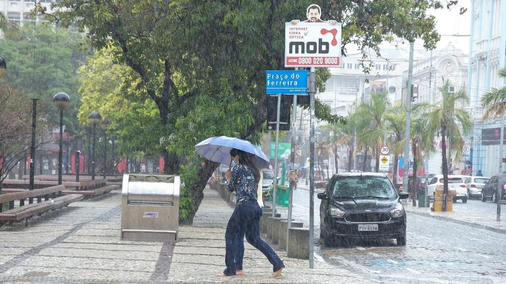 Duas mulheres dividem um guarda-chuva e apressam os passos para se esquivar da chuva na Praça do Ferreira, em Fortaleza