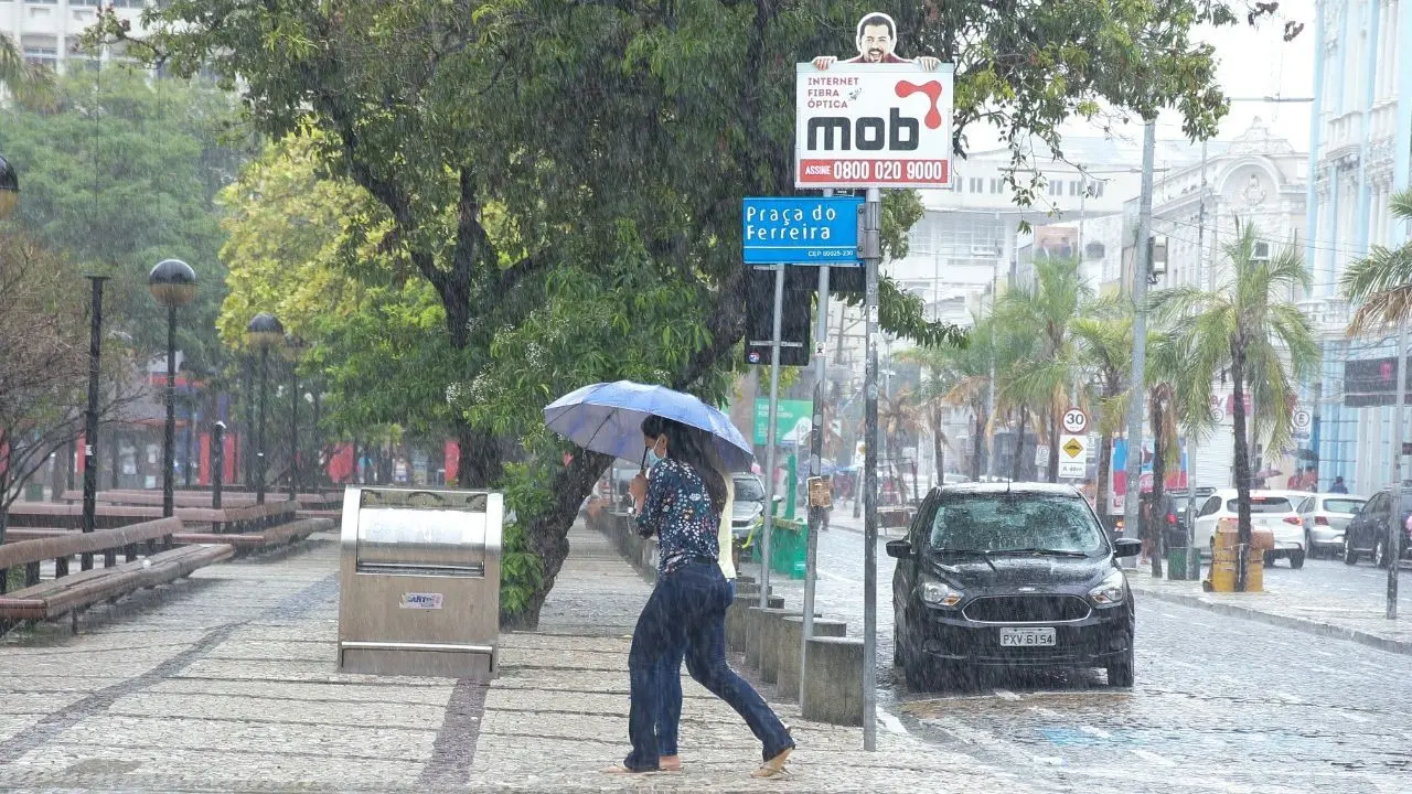 Duas mulheres dividem um guarda-chuva e apressam os passos para se esquivar da chuva na Praça do Ferreira, em Fortaleza