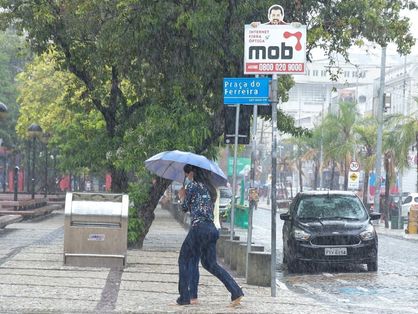 Duas mulheres dividem um guarda-chuva e apressam os passos para se esquivar da chuva na Praça do Ferreira, em Fortaleza
