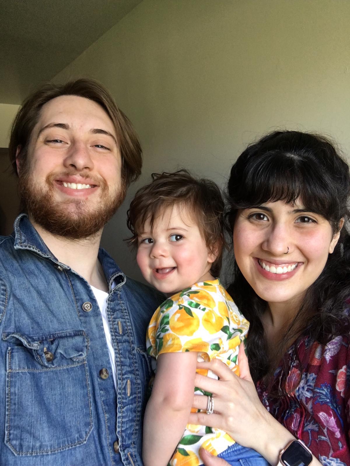 Foto de família composta por um homem, uma mulher e um bebê posando para a foto sorrindo