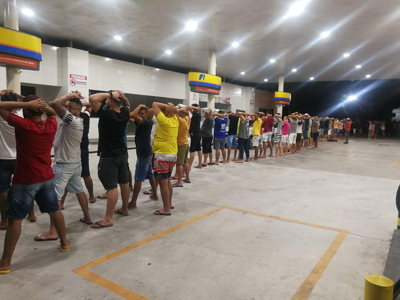 Pessoas enfileiradas com as mãos na cabeça para revista policial