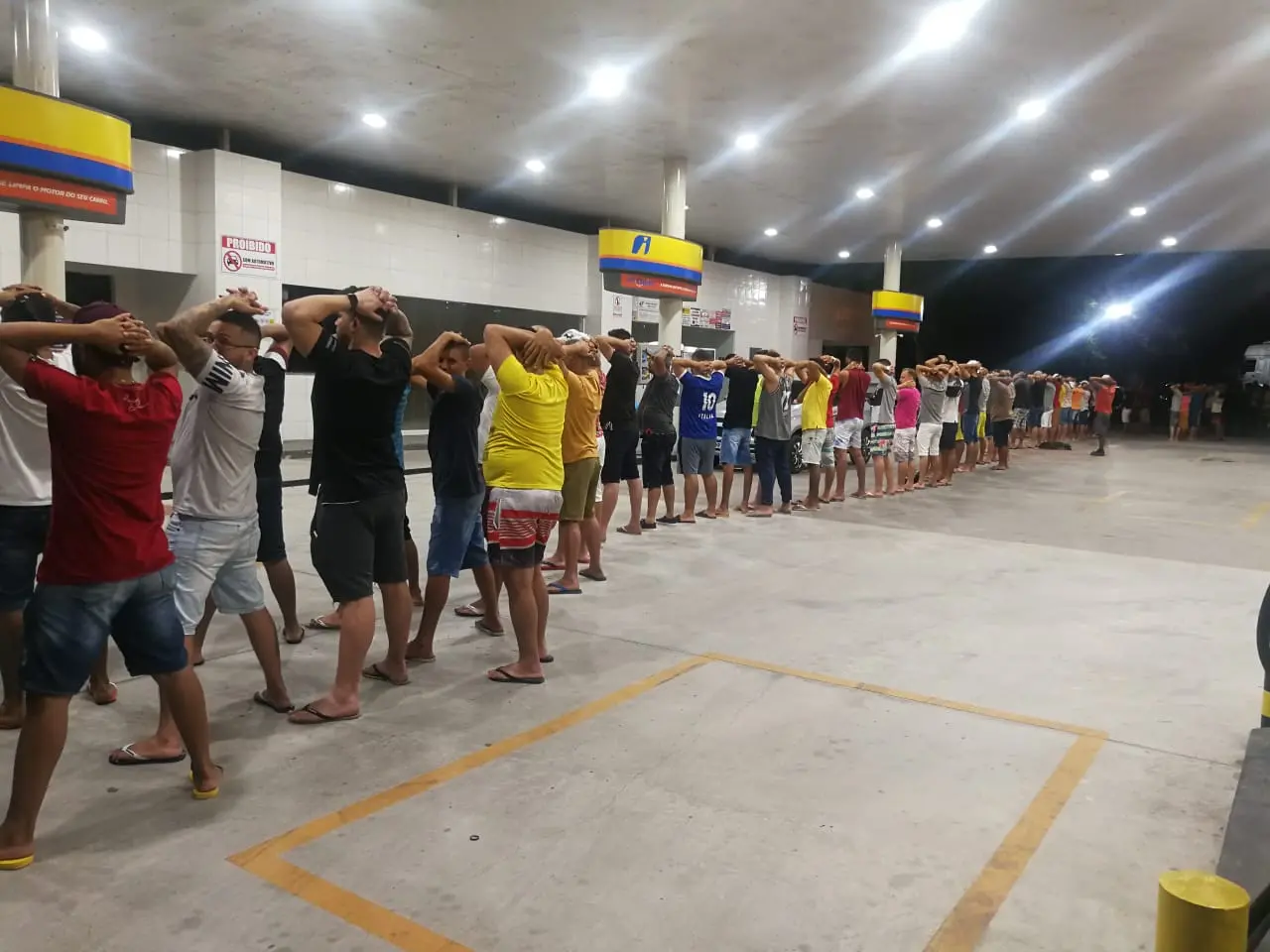 Pessoas enfileiradas com as mãos na cabeça para revista policial