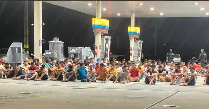 Pessoas sentadas no chão em posto de combustível