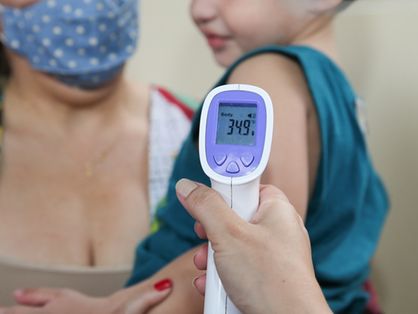 Medidor de temperatura sendo colocado em braço de criança