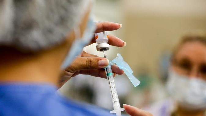 Profissional da saúde aplica prepara seringa para aplicar vacina.