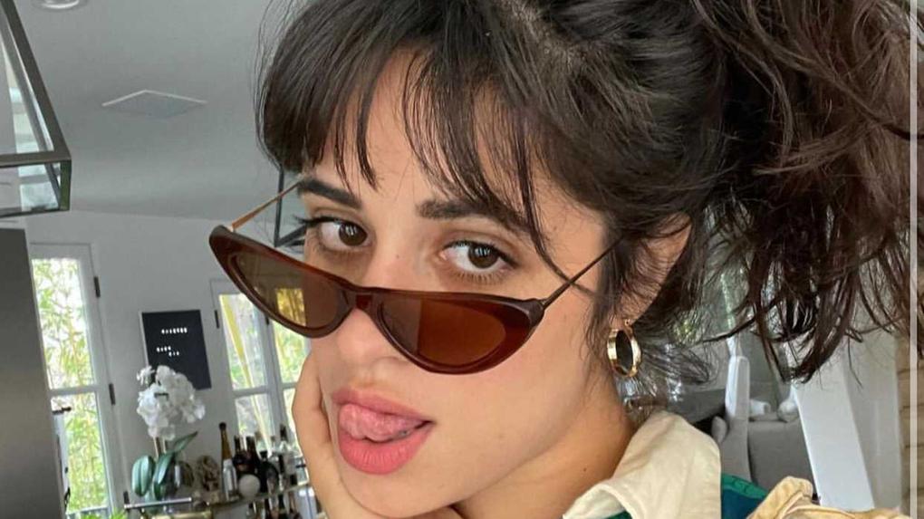 Foto da artista Camila Cabello, com óculos escuros e mostrando a língua