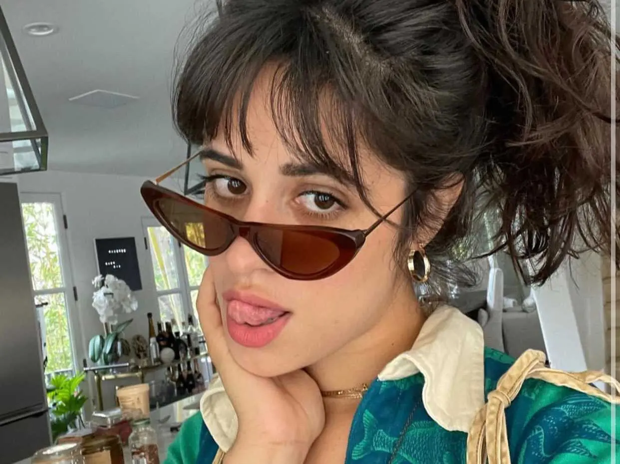 Foto da artista Camila Cabello, com óculos escuros e mostrando a língua