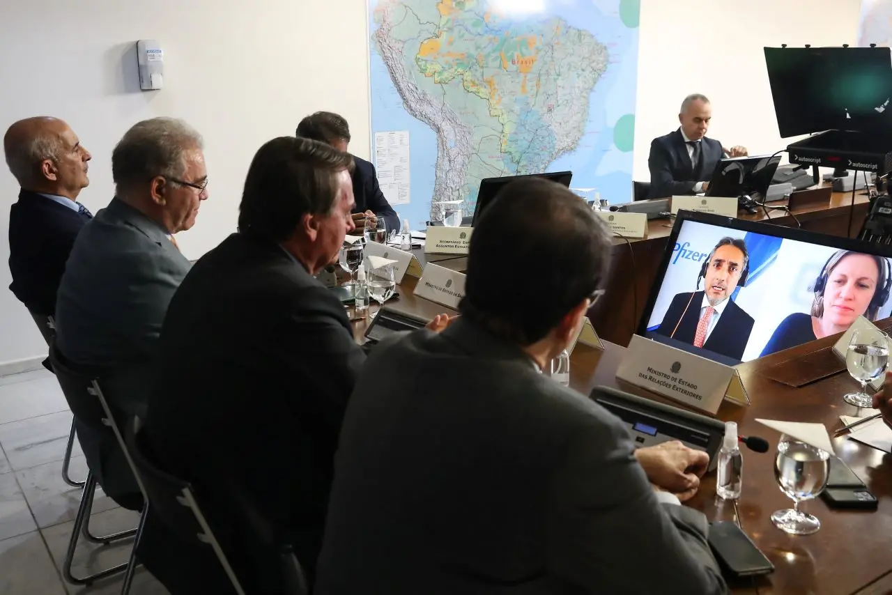 presidente e ministros diante de tela onde aparecem representantes da pfizer participando por videoconferência da reunião