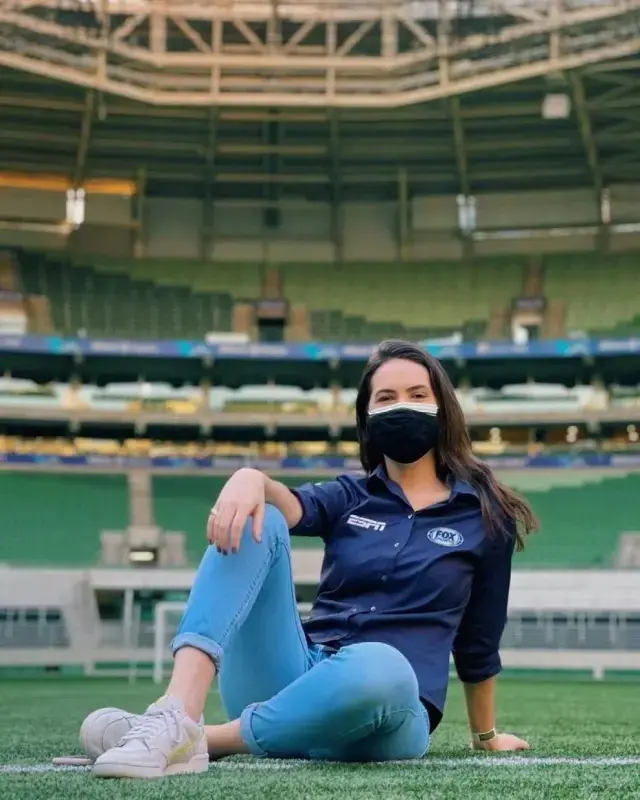 Jornalista sentada num gramado de campo de futebol