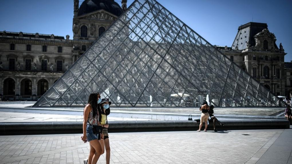 Turistas usando máscara de proteção contra a Covid-19 passeiam em frente ao museu do Louvre, em Paris, França