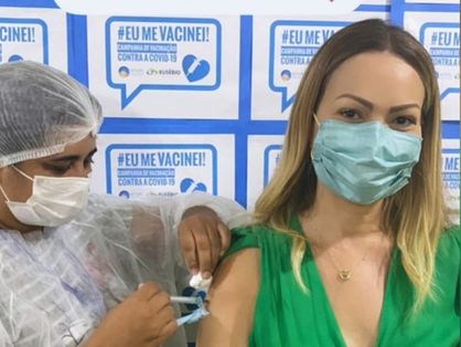 Solange Almeida de vestido verde sendo vacinada contra a Covid-19