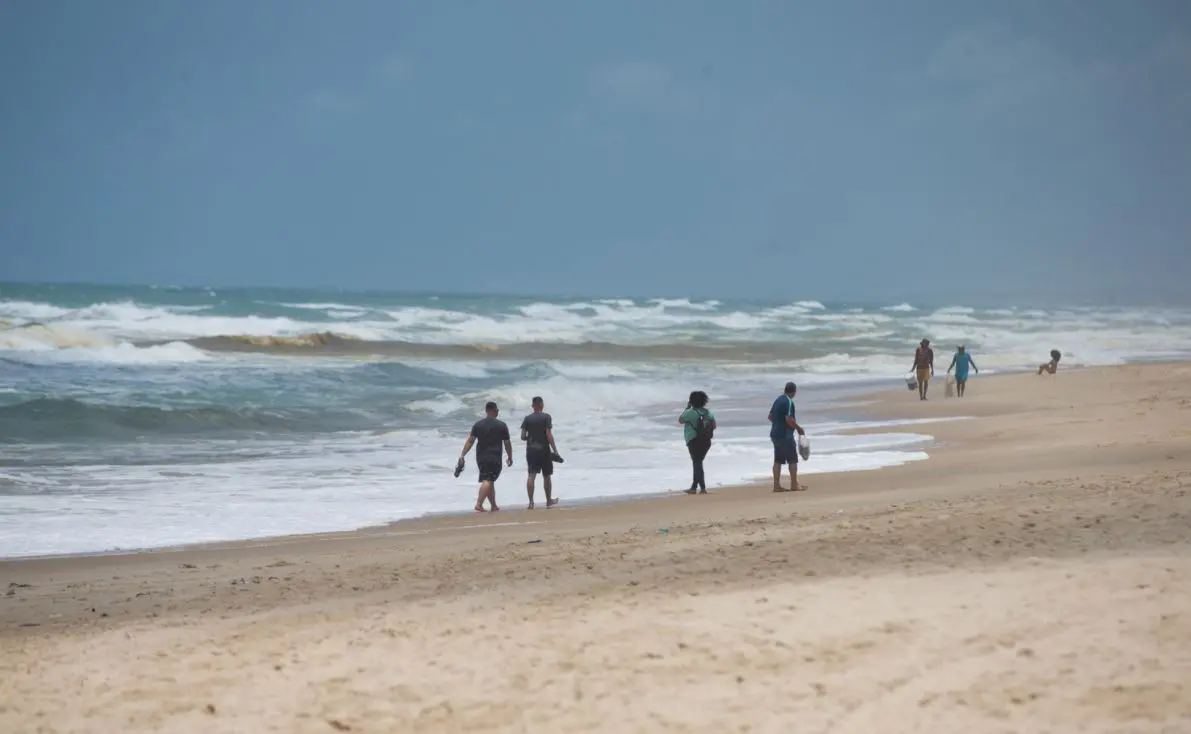 Praia com céu claro e poucas pessoas na faixa de areia