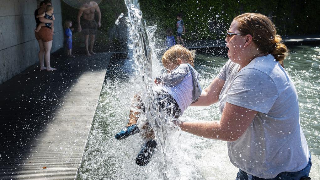 Uma mulher segura uma criança sob uma cachoeira em um parque em Washington, DC, em 28 de junho de 2021