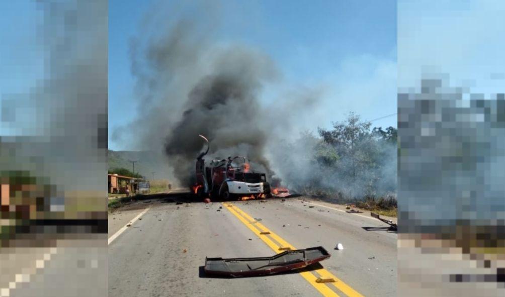 Imagem mostrando carro-forte pegando fogo em rodovia, com fumaça saindo do veículo e destroços na pista