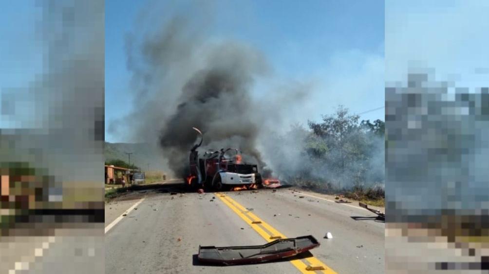 Imagem mostrando carro-forte pegando fogo em rodovia, com fumaça saindo do veículo e destroços na pista