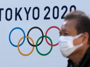 Pessoa com máscara na frente de símbolo dos Jogos Olímpicos de Tóquio