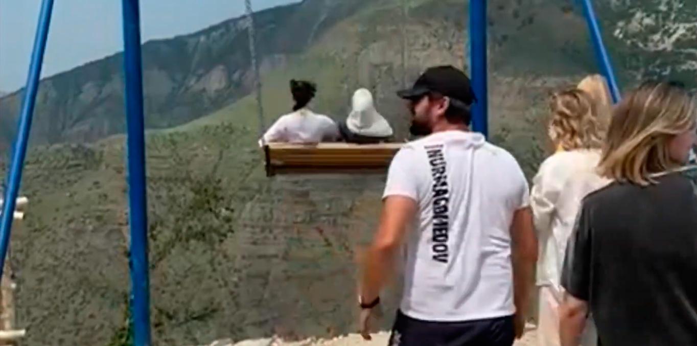 Duas jovens estão no balanço enquanto pessoas olham para os lados