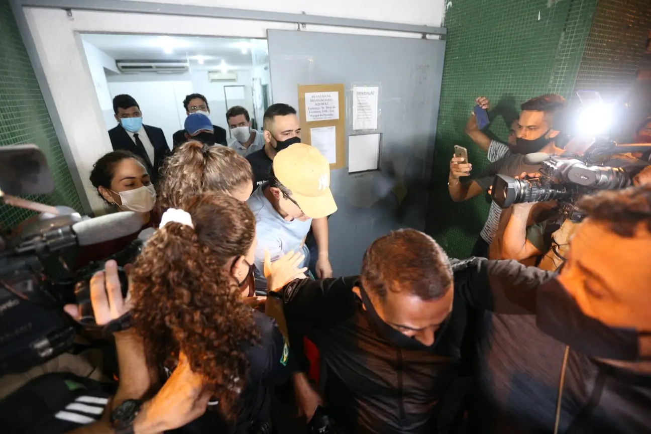 de boné, dj ivis deixa a delegacia metropolitana do eusébio cercado por policiais e profissionais da imprensa