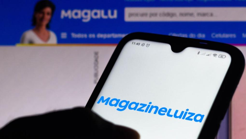 Celular com logo do Magazine Luiza em frente a PC com site do Magalu aberto
