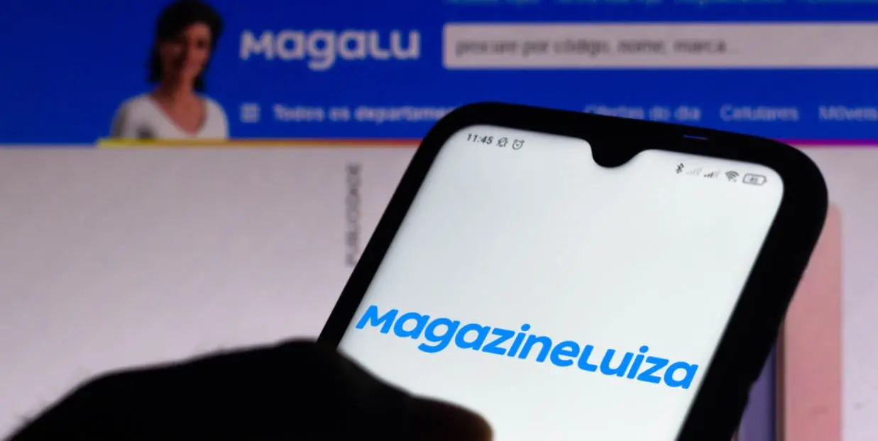 Celular com logo do Magazine Luiza em frente a PC com site do Magalu aberto