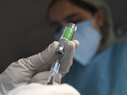 Mão segurando frasco da vacina da AstraZeneca e retirando conteúdo com seringa