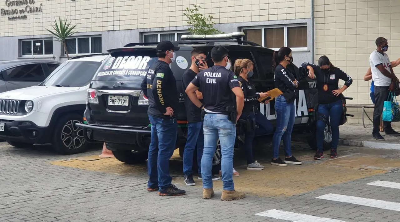 Agentes da Polícia Civil parados ao lado de viatura