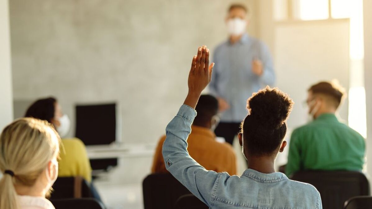 Estudante negra com mão levantada em sala de aula com outras pessoas