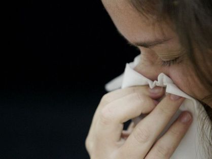 Pessoa espirrando e com lenço no nariz