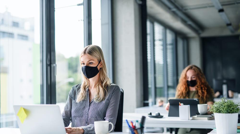 Mulheres de máscara trabalhando em escritórios