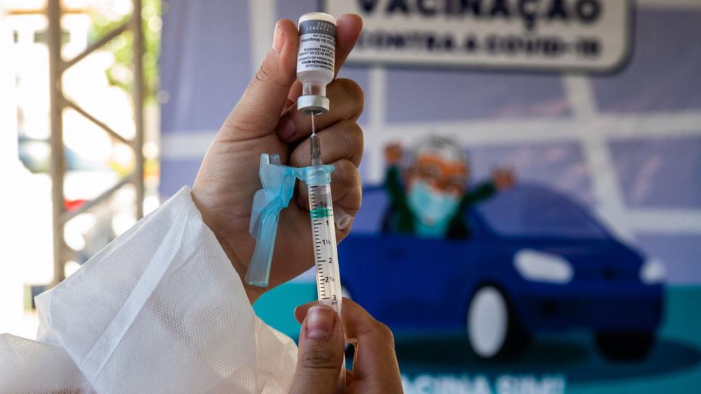 Mão segurando vacina contra Covid-19 e seringa