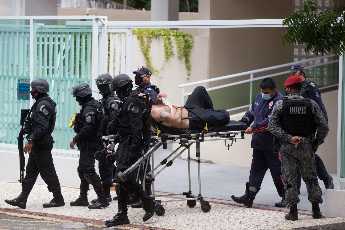 guarda municipal que manteve mãe e irmão reféns saindo de apartamento algemado em maca escoltado por policiais