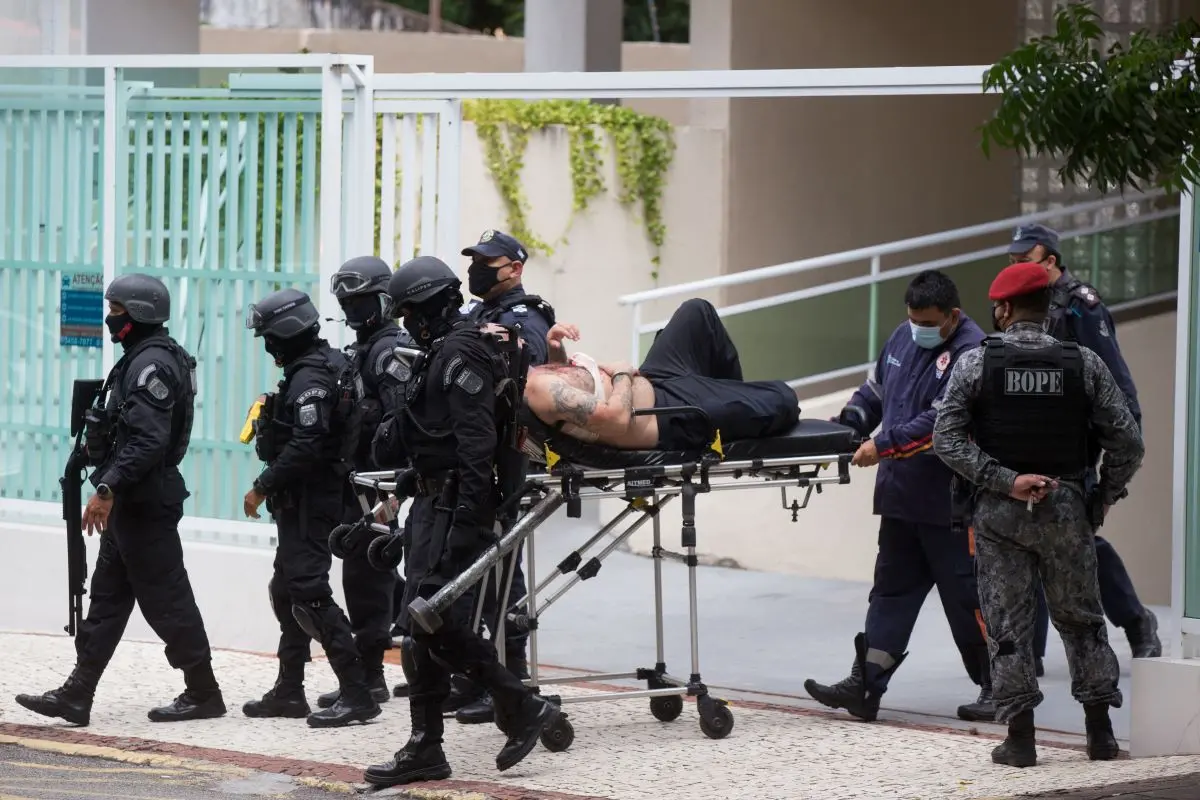 guarda municipal que manteve mãe e irmão reféns saindo de apartamento algemado em maca escoltado por policiais