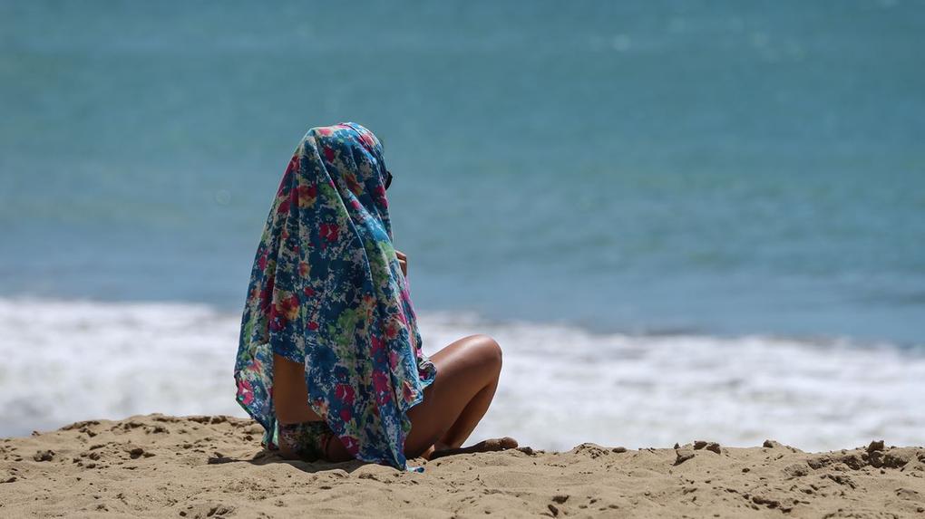 Pessoa sentada em praia coberta com tecido sob sol forte