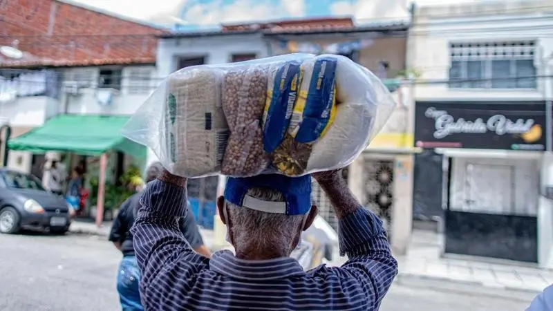 Idoso carregando cesta básica sobre a cabeça