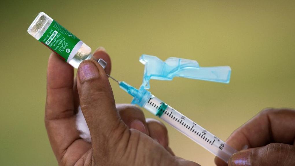 Pessoa segura seringa fincada em frasco de vacina da CoronaVac