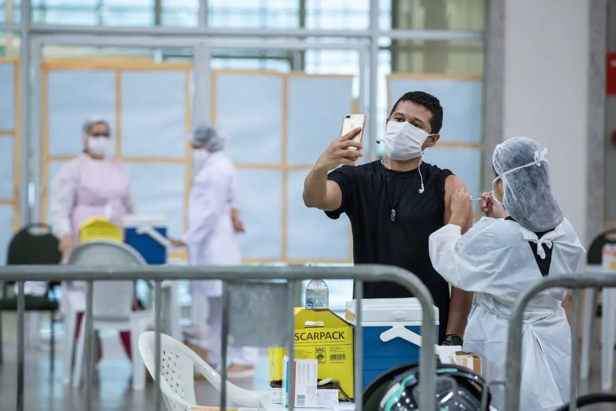 Homem tirando foto enquanto recebe vacina contra a Covid-19