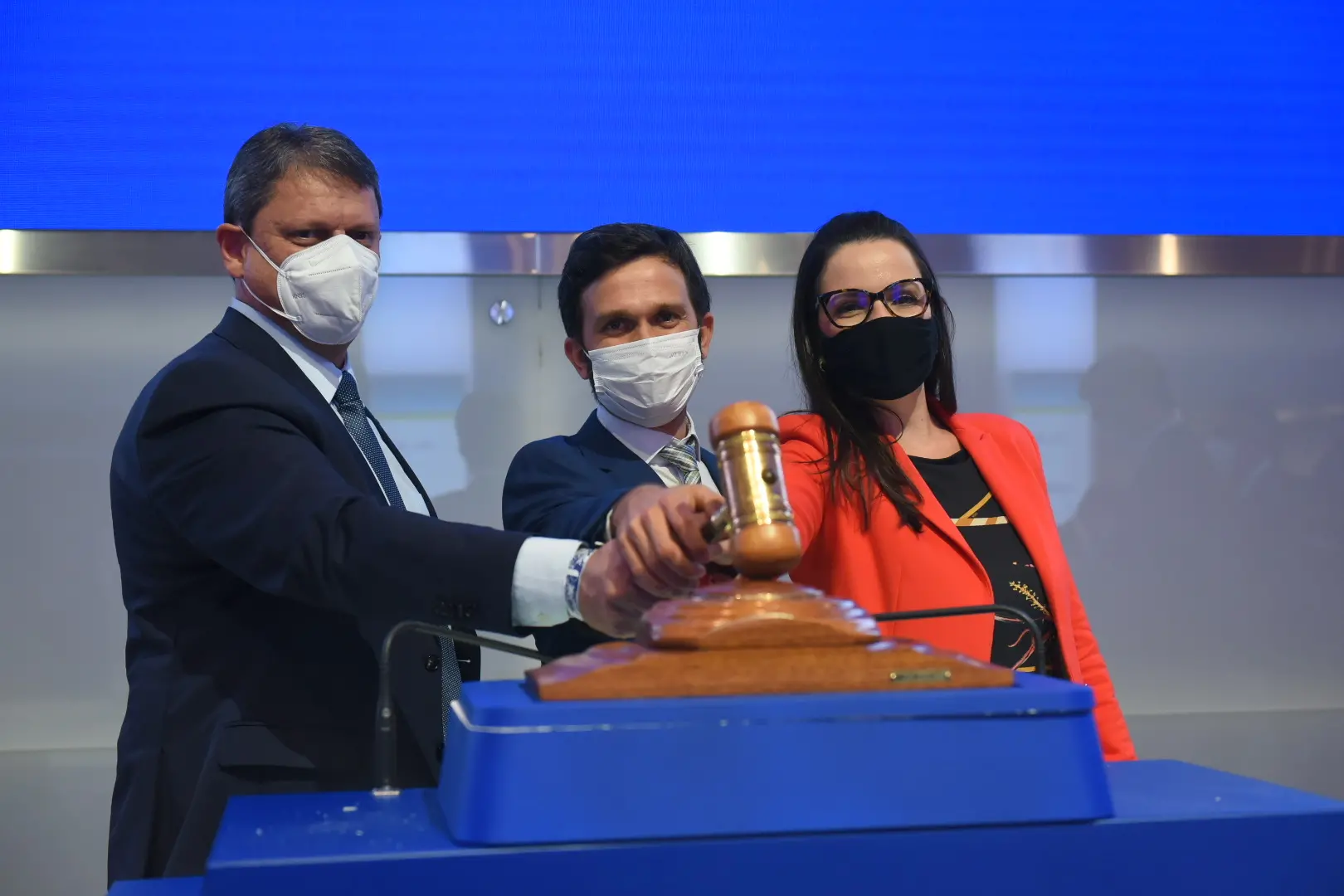 Dois homens e uma mulher batendo um martelo de leilão