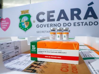 Três doses de vacina em cima de caixa com logo do butantan. O fundo, logo do governo do estado do Ceará