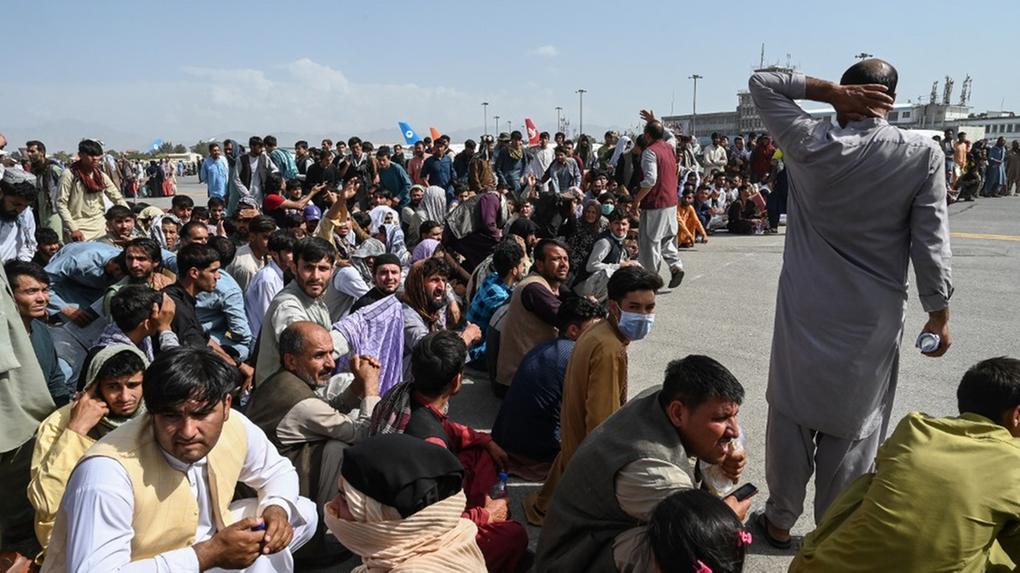Multidão de homens sentada em pista de aeroporto no Afeganistão