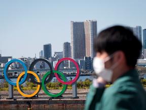 Imagem de uma residente de Tóquio com máscara na frente do símbolo olímpico