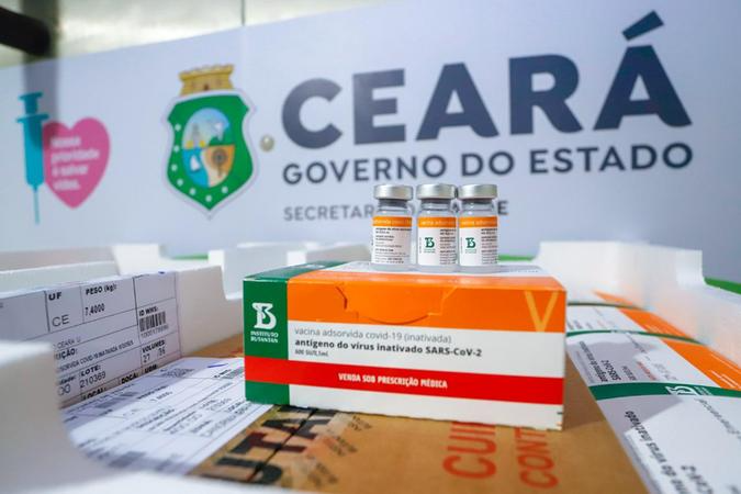 Caixa com doses de CoronaVac com letreiro do governo do Ceará ao fundo