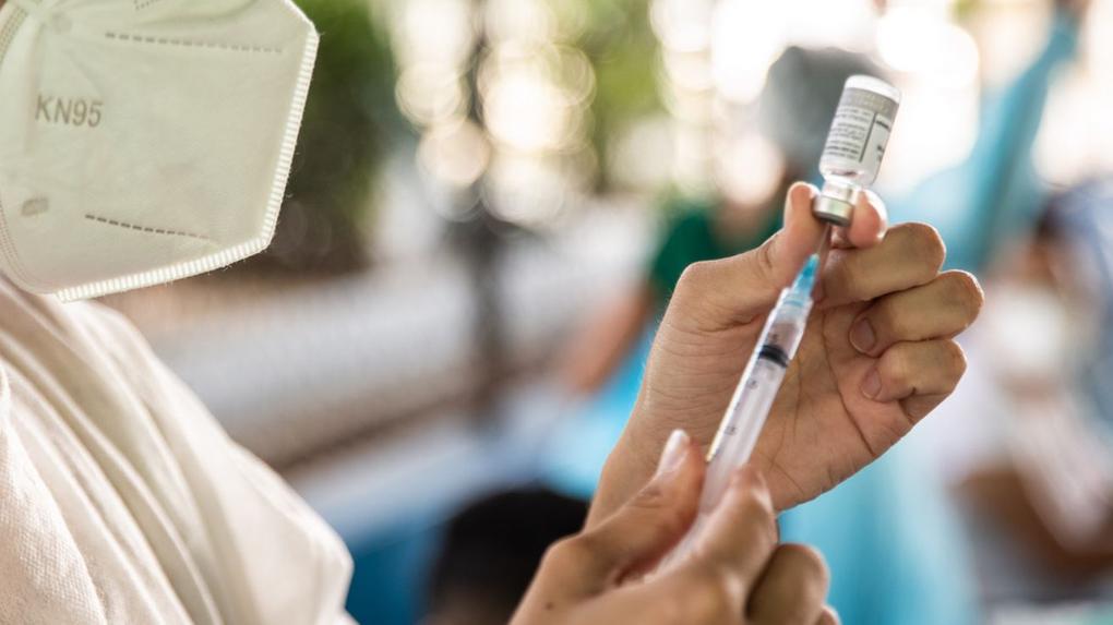 Mão segurando vacina e seringa com dose de imunizante contra Covid-19