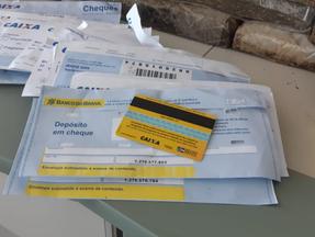 Cartão do auxílio emergencial sobre envelopes da Caixa e com drogas ao redor