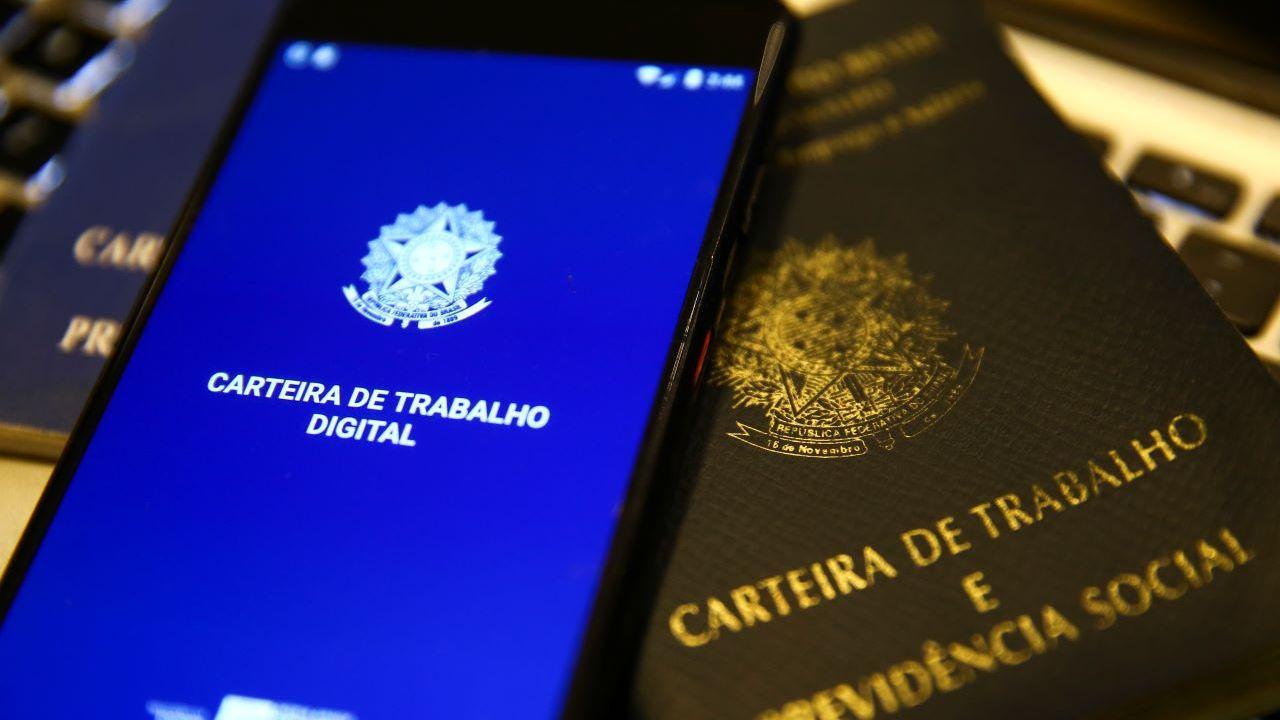 Carteira de trabalho física e celular com aplicativo da carteira de trabalho aberto sobre a mesa